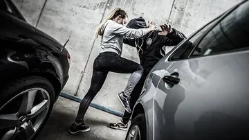 Woman self-defends against hooded man near cars.