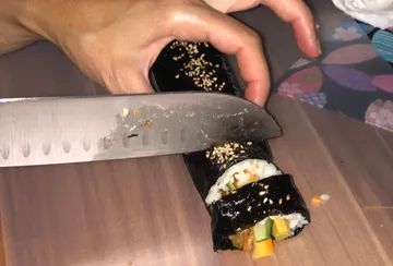 Hand slicing sushi roll on wooden surface.