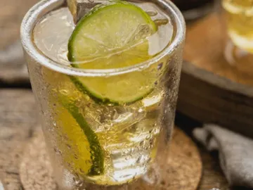 Glass with drink, ice and lime slices on wooden background.