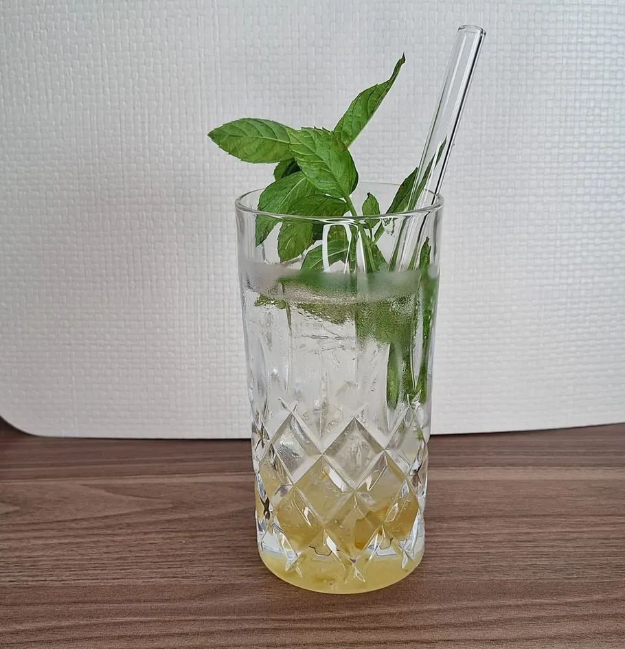 Glas mit Minzblättern, Strohhalm, Holztisch.