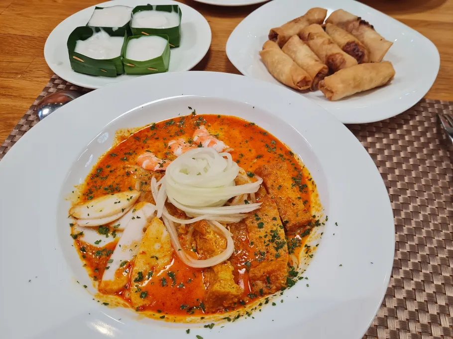Soup with seafood, spring rolls, and desserts on table.