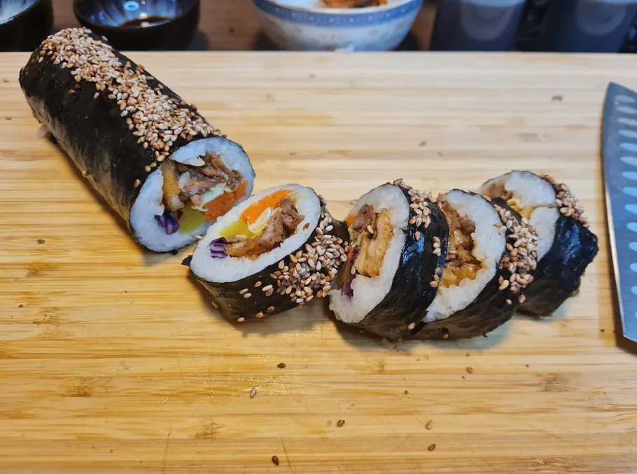 Sliced sushi roll with sesame on wooden board.