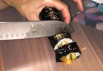 Hand schneidet Sushirolle auf Holzbrett.