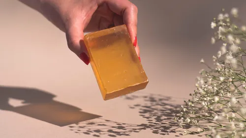 Hand hält orangefarbene Seife nahe Blumen.