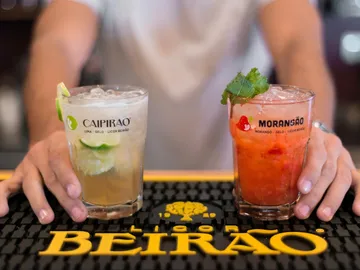 Zwei Cocktails werden von Händen auf einer Theke gehalten.