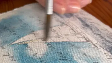 Hand painting blue text on paper.
