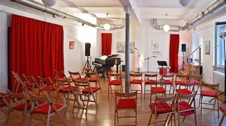 Leerer Musikraum mit roten Vorhängen und Stühlen.
