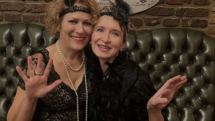 Zwei lächelnde Frauen in Vintage-Outfits drinnen.