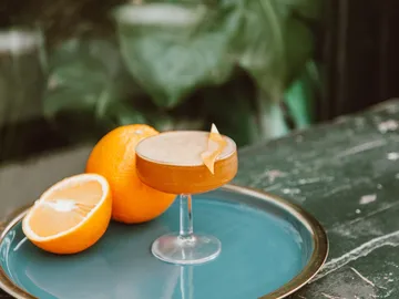 Ein Cocktailglas steht auf einem Tablett mit Orangen.