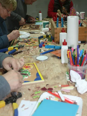 People creating mosaics on a cluttered table.