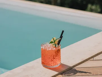 Getränk mit Eis steht neben einem blauen Schwimmbad.
