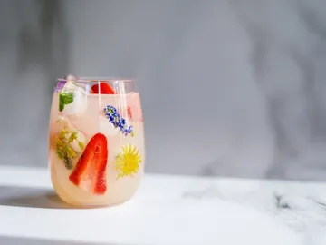 A glass of drink filled with fruits and herbs.