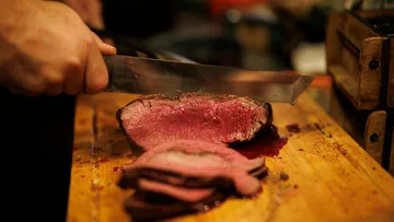 Person slicing roast beef on wooden board.