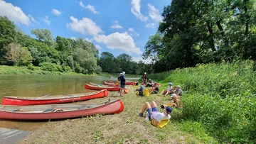 People resting by canoes on riverbank.