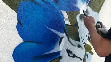 Person sprüht blaue Blumenmural.