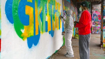 Zwei Personen sprühen Graffiti an Wand innen.