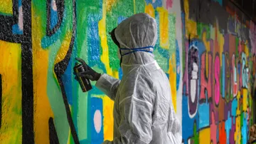 Person spray-paints colorful graffiti on wall.