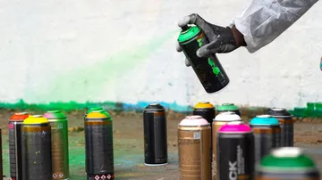 Hand spray-painting, surrounded by paint cans.