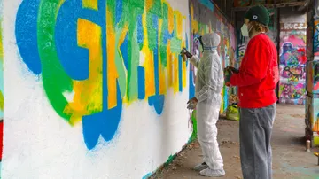 Two people spray painting colorful graffiti wall.