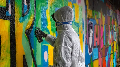 Person in coveralls spray-paints colorful graffiti wall.