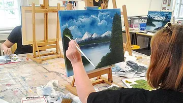 Woman painting landscape on canvas in classroom.