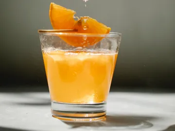 Ein Glas mit orangefarbigem Getränk und Orangenscheibe.