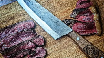 Sliced steak and knife on wooden board.