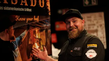 Mann zeigt auf Grillfest-Poster drinnen.