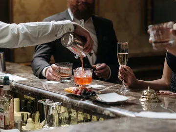 Barkeeper gießt Cocktail an eleganter Bar mit Gästen.