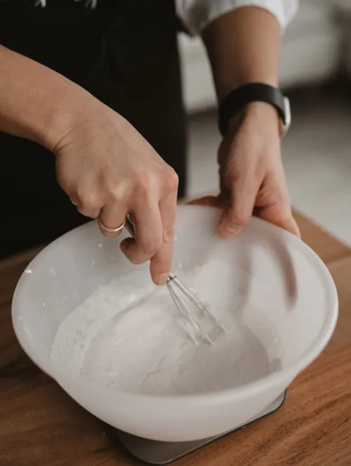 Hand whisking mixture in a white bowl.