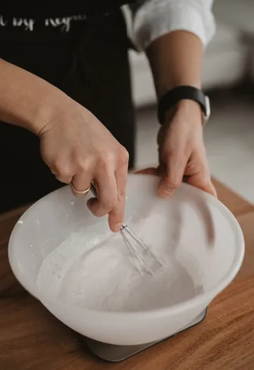 Person whisking batter in white bowl on table.