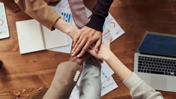 Hands stacked in unity over desk.