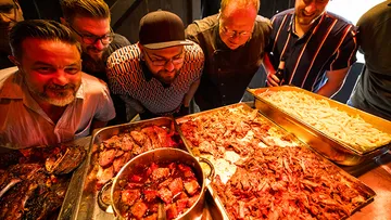 Group admiring various cooked meats on trays.