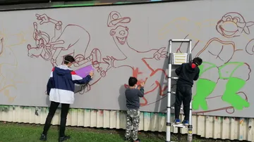 Drei Personen malen bunten Cartoon-Wandbild.