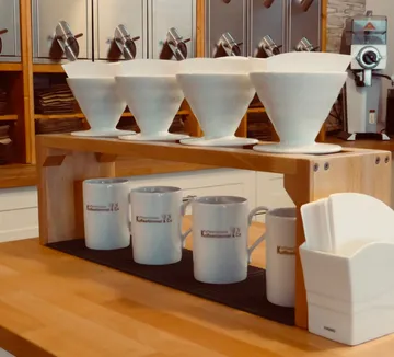 Coffee drippers on shelf above mugs in cafe.