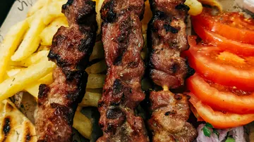Gegrillte Spieße mit Pommes und Tomaten auf Teller.