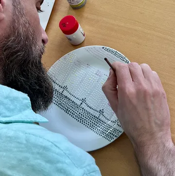 Person painting dots on ceramic plate.