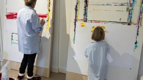 Zwei Personen malen auf großen Leinwänden drinnen.