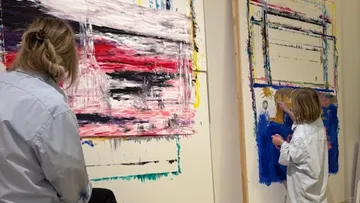 Two people painting on large canvases indoors.