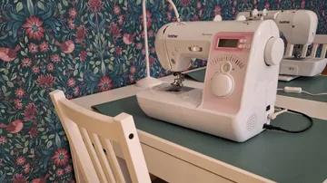 Nähmaschine auf Tisch, florale Wandtapete.