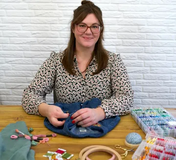 Frau stickt Stoff auf Holztisch.