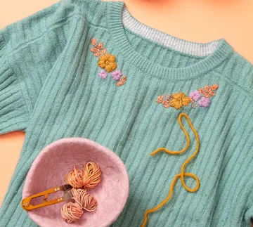 Bestickter Pullover mit Garn und Schale auf Tisch.