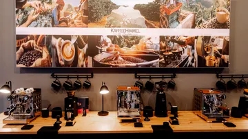 Espressomaschinen auf Holztresen unter Kaffeecollage.