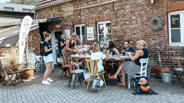 Gruppe bastelt an einem Tisch vor Backsteingebäude.