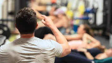 Instructor pointing, people exercising in gym.