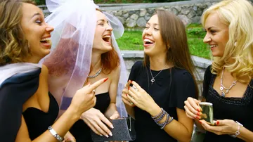 Four women laughing outdoors, one in veil.
