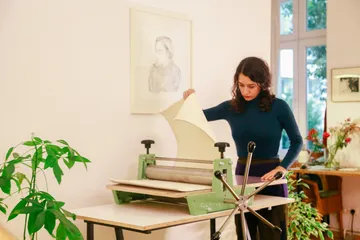 Frau nutzt Druckpresse im Atelier mit Pflanzen.