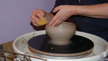 Hands shaping clay bowl on pottery wheel.