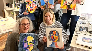 Group displaying colorful abstract face paintings indoors.