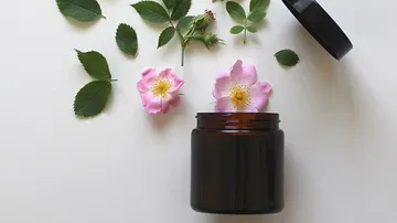 Offenes Glas mit Blumen und Blättern daneben.